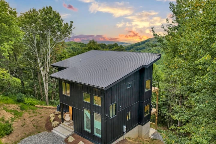 Modern dark-sided mountain home surrounded by trees at sunset