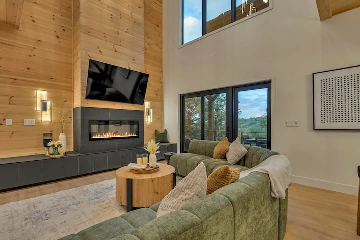 Double-height living room with a fireplace, timber ceiling, and large windows